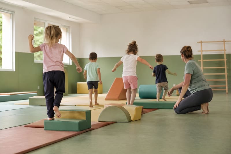Jeunes enfants sur un parcours de motricité en mousse, accompagnés d'une animatrice