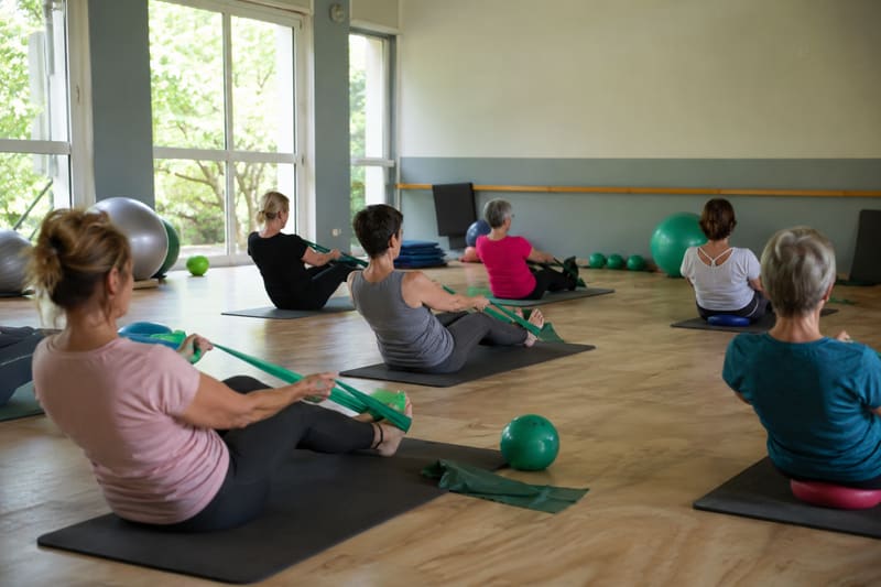 Cours de Pilates au sol, avec élastiques et ballons, dans une salle claire